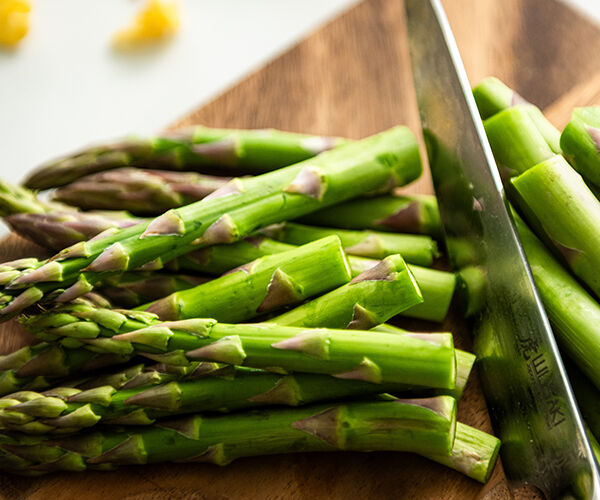 découpe d'asperges verte sur une planche en bois avec un couteau de cuisine